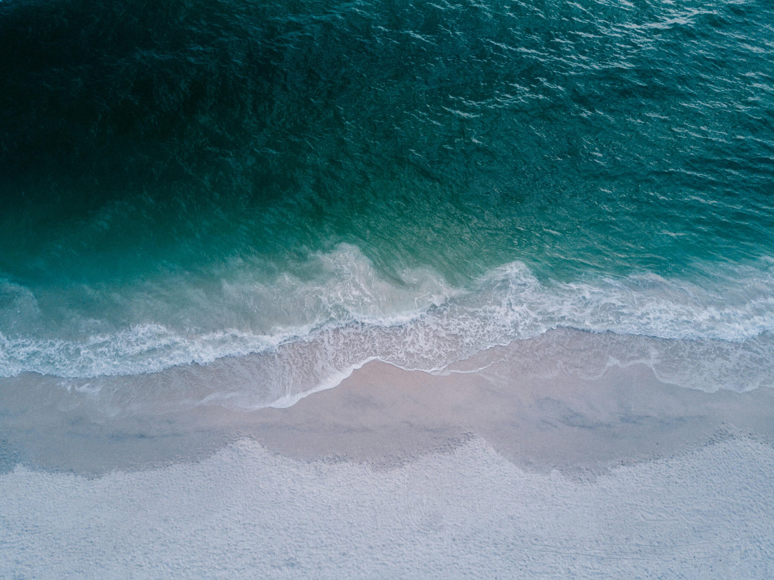 Stunning aerial shot of turquoise ocean waves washing onto a pristine sandy beach, perfect for backgrounds.